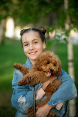 A cute teen girl on a walk with toy poodle dog. It's spring outside. The girl is dressed in a blue jacket in a flower and jeans. Childhood. Pets.