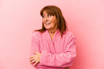 Middle age caucasian woman wearing a bathrobe isolated on pink background looks aside smiling, cheerful and pleasant.