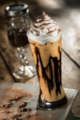 Cappuccino milkshake with whipped cream on top and chocolate syrup, on a wooden table