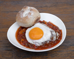 Winter food. Closeup view of a lentil stew with vegetables, a grilled egg and country bread, in a white bowl on the restaurant wooden table. 