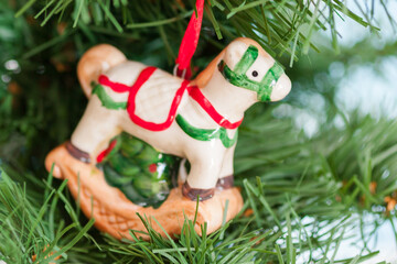 Closeup of a ceramic Christmas toy, little horse, on the branch of a spruce. New year decoration, winter holidays background