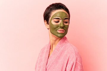 Young caucasian woman wearing a face mask isolated on pink background looks aside smiling, cheerful and pleasant.