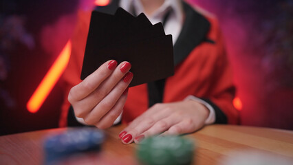 Headless blonde anime school girl hold black poker cards in hand with betting chips out of focus