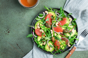 Healthy vegan salad with arugula, avocado, juicy grapefruit, cashews and dressing with olive oil, honey and wine vinegar. Green rustic kitchen table, top view, copy space