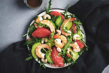 Fresh summer salad with shrimps, avocado, pink grapefruit, arugula and cashews. Gray stone kitchen table background, top view, copy space