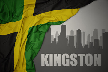 abstract silhouette of the city with text Kingston near waving national flag of jamaica on a gray background. 3D illustration