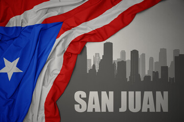 Obraz na płótnie Canvas abstract silhouette of the city with text San Juan near waving national flag of puerto rico on a gray background. 3D illustration