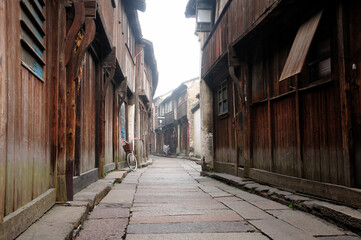 Fototapeta premium Wooden, weathered buildings lining a narrow walkway in tongxiang wuzhen scenic town east view in Zhejiang province China in the early morning mist.