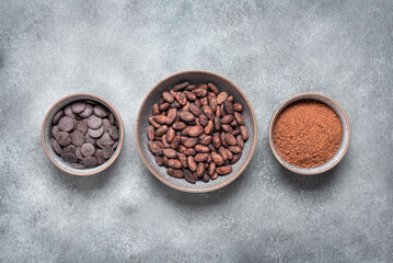Cocoa beans, cocoa powder and chocolate in a bowl, grunge gray background. Top view, copy space