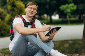 Naklejka na ściany i meble Young smiling student outdoors with tablet. The concept of college education