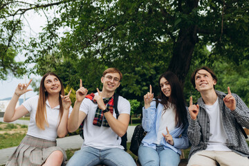 Group of student friends pointing up at copy space in park