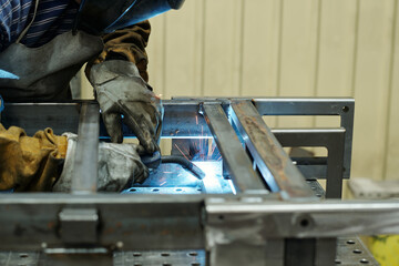 Gloved hands of male worker of industrial plant producing huge machines bending over workbench and welding metallic parts