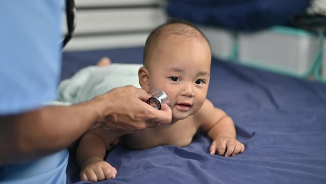 Asian Pediatrician doctor examines baby boy with stethoscope checking heart beat.