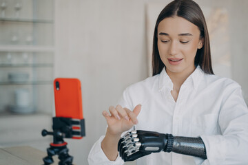 Pretty disabled girl is blogger. Amputee is taking video how to use mechanical cyber arm.