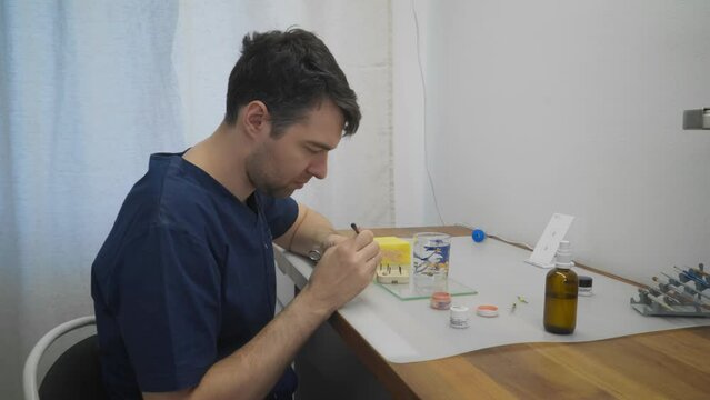 Technician is painting the metal dental crowns at a clinic. Dental technician is painting the teeth with the brush. Dental technician is painting the tooth before the artificial jaw assembly