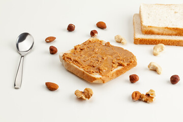 Square bread for toast with peanut butter. Nuts, spoon, bread slices and a peanut butter sandwich on a white table. - 515014541