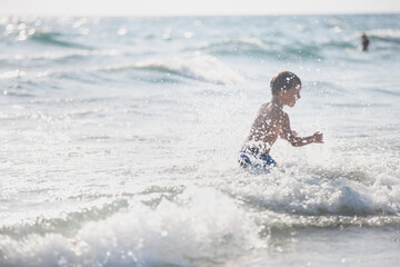 A little boy on the beach, playing with the waves, summer time. Concept of relaxation and a healthy lifestyle