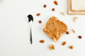Square bread for toast with peanut butter. Nuts, spoon, bread slices and a peanut butter sandwich on a white table.