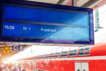 Close-up sign data information timetable digital display board against fast moving modern regional red double decker express train at sunset on german railway platform. Railroad travel ticket concept