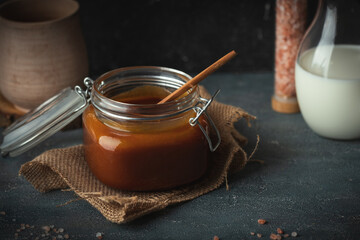 Brown salted caramel in a glass jar on burlap on a black background
