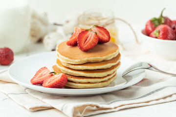 American pancakes stacked in a pile decorated with strawberries in a white plate. Healthy and tasty breakfast