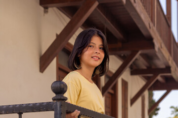 A teenage girl stands on the balcony of a country house.