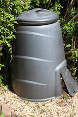 A plastic compost bin in an English garden. Garden and vegetable waste is emptied into the top and rotted compost can be removed from the bottom