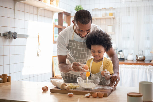 Smiling Black African American Father and little son baking together in kitchen at home