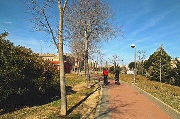 Ciclistas practicando deporte en una soleada mañana de invierno. Carril bici (ruta circular de Madrid) en el barrio de Las Tablas de Madrid, España. - obrazy, fototapety, plakaty
