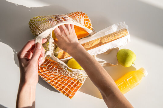 Women's Hands Take Out Food From A Shopping Bag On A White Table. Top View, Flat Lay.