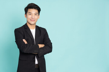 Obraz na płótnie Canvas Smiling young Asian businessman with arms crossed isolated on green background