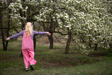 Young girl is dancing with hands up near flower trees in the garden during blooming time.