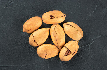 Small pile of inshell pecans on a dark background, top view