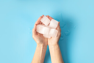Woman's hand holding ice cubes on blue background. Top view, flat lay