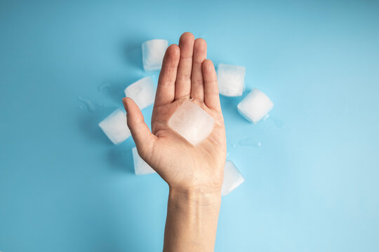 Woman's hand holding an ice cube on a blue background. Top view, flat lay