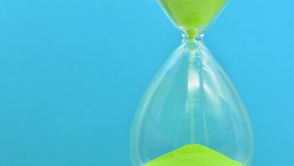 Detalle de un reloj de arena verde contando el tiempo - obrazy, fototapety, plakaty