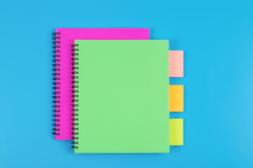 Colourful notebooks and sticky notes arranged on blue background, top view.
