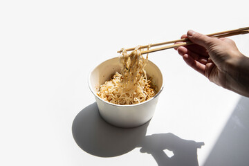 Female hands hold chinese chopsticks picking noodles in a cardboard bowl on a white background