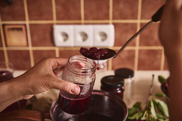 Details: Hands of confectioner pouring delicious freshly made cherry berry jam into sterilized...