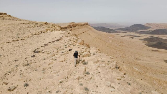 A drone flying over a man as it travels along the edge of the Ramon crater