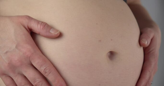 Woman running her hands over her pregnant belly. Macro close up, gimbal