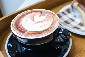 Hot chocolate in black ceramic cup with heart-shaped latte art pattern from milk foam.