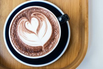Hot chocolate in black ceramic cup with heart-shaped latte art pattern from milk foam.