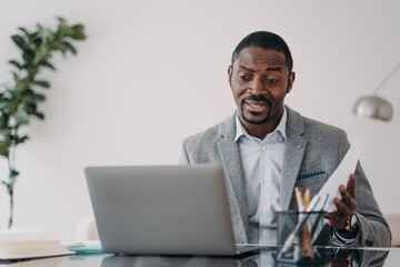 Perplexed african american businessman looking at laptop screen reading bad news in email at desk