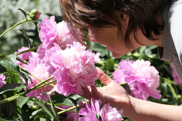 In summer, a girl admires beautiful flowers in a flower bed.