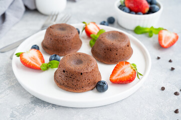 Chocolate fondant lava cake with fresh berries on a plate on a gray background.