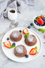 Chocolate fondant lava cake with fresh berries on a plate on a gray background.