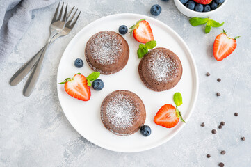 Chocolate fondant lava cake with fresh berries on a plate on a gray background.
