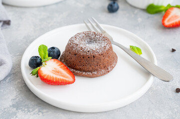 Chocolate fondant lava cake with fresh berries on a plate on a gray background.