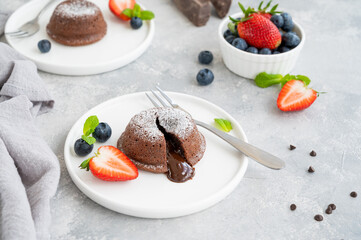 Chocolate fondant lava cake with fresh berries on a plate on a gray background.